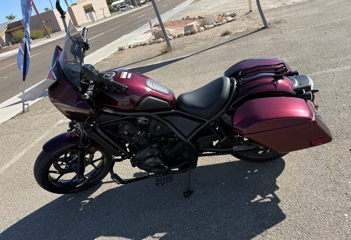 A maroon and black Honda Rebel 1100 DCT motorcycle with saddlebags, parked on an asphalt lot available for consignment purchase.