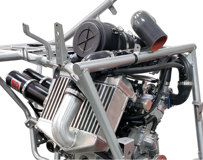 A close-up of a high-performance engine with a silver metal tubular frame, black air filter, polished silver intake manifold, and black exhaust pipes on a white background.